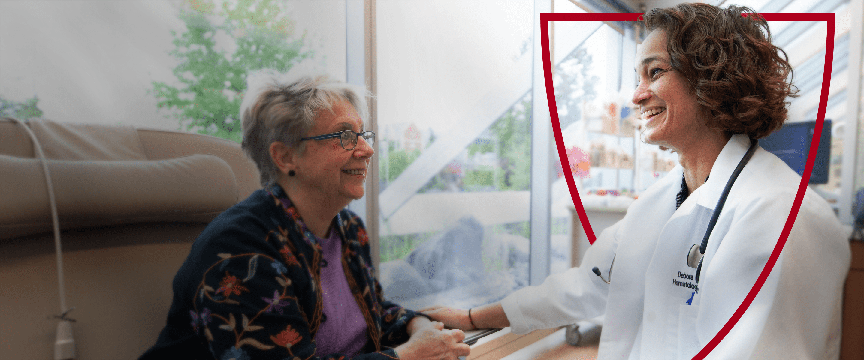 A smiling female doctor and elderly patient talking in a bright medical setting.