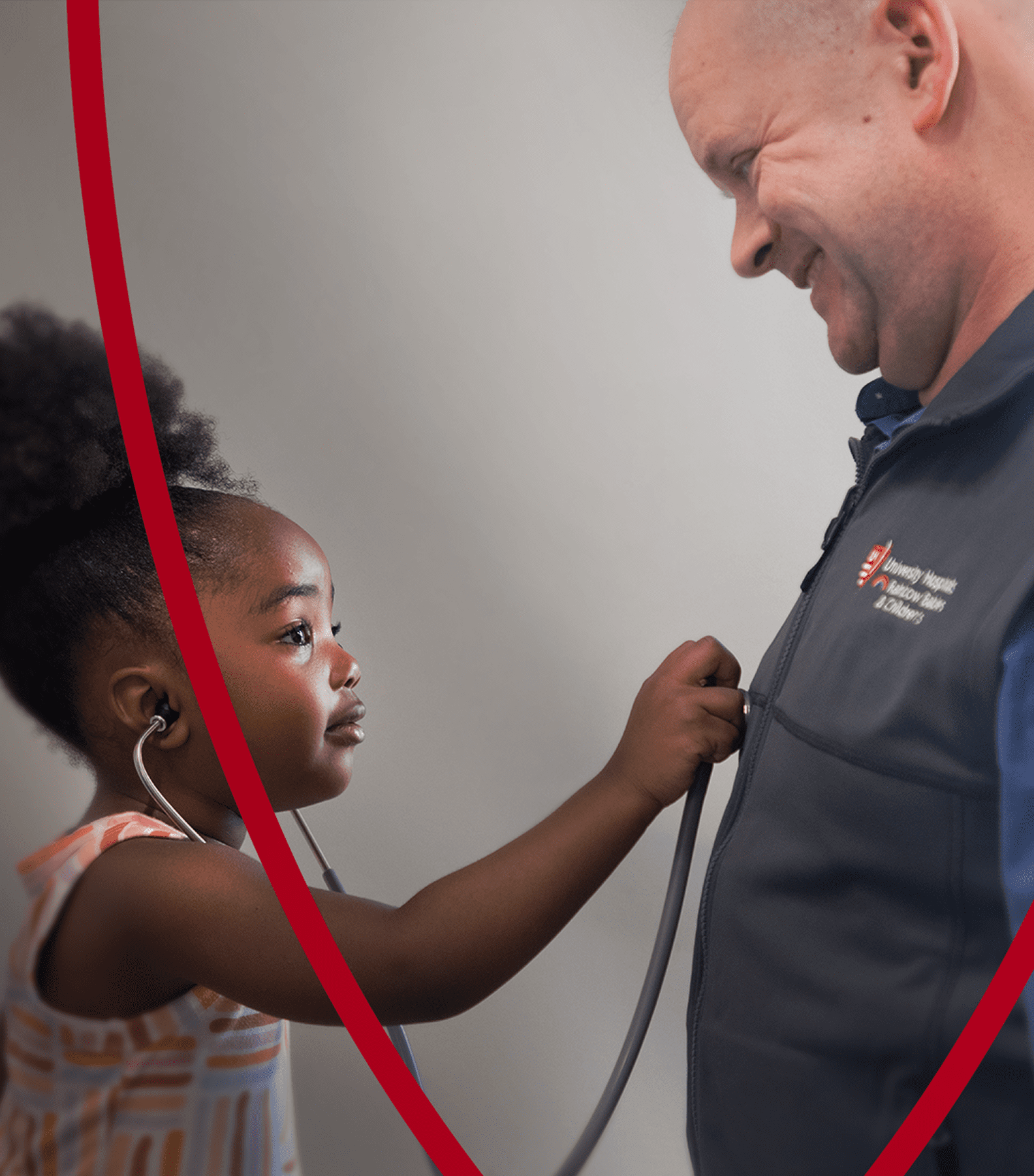 A young girl uses a stethoscope to listen to a smiling healthcare professional’s heartbeat, creating a heartwarming moment.