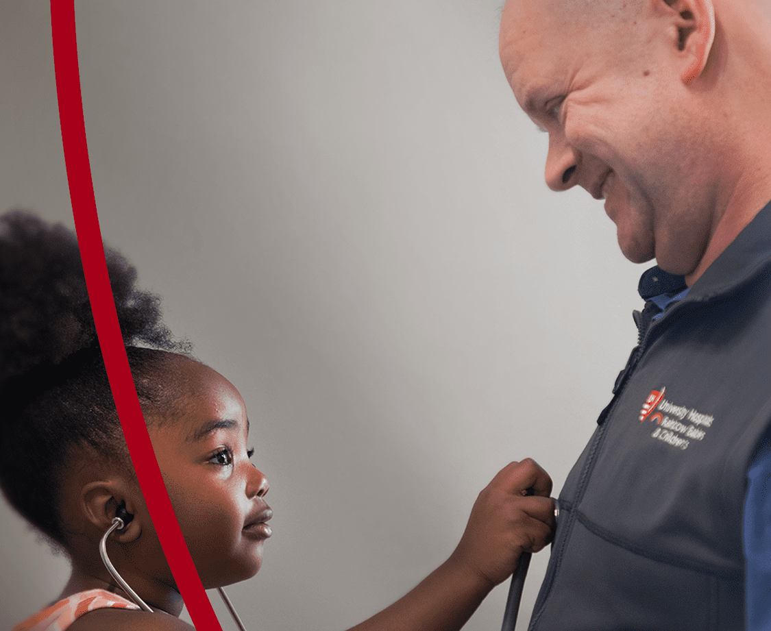A young girl uses a stethoscope to listen to a smiling healthcare professional’s heartbeat, creating a heartwarming moment.