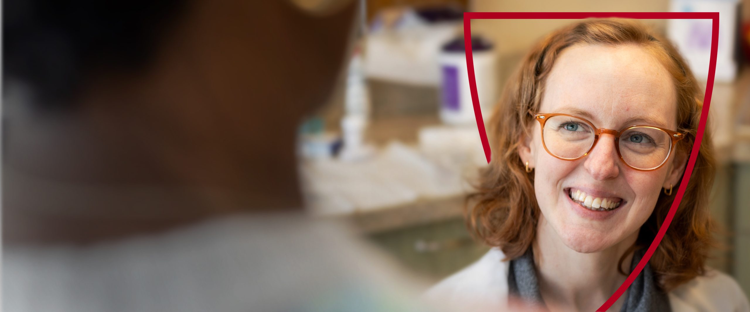 A smiling healthcare professional in glasses interacts with a patient.