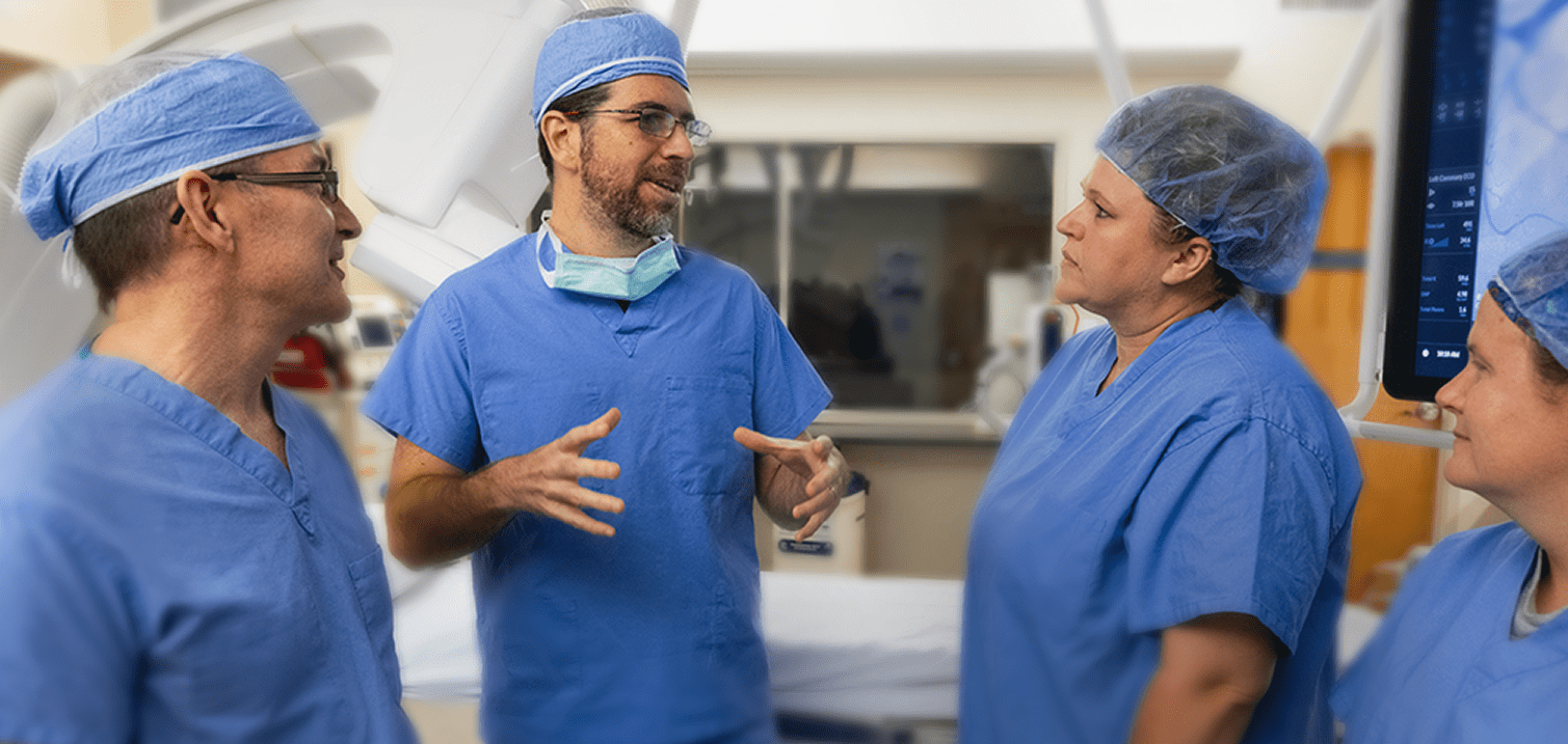A group of healthcare professionals in blue surgical scrubs engaged in discussion in a medical setting.