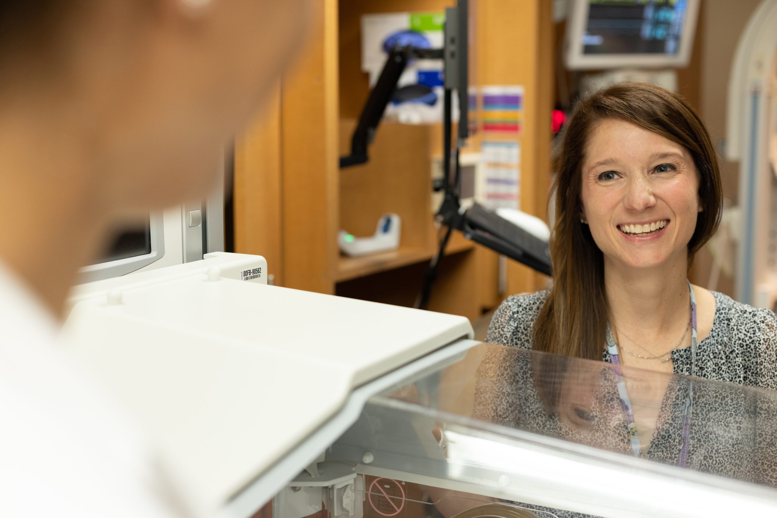 dd2a3db1fbf5219f258224d95a7e519b4bfda88c A smiling healthcare professional behind a counter engages with a colleague in a welcoming medical office setting.
