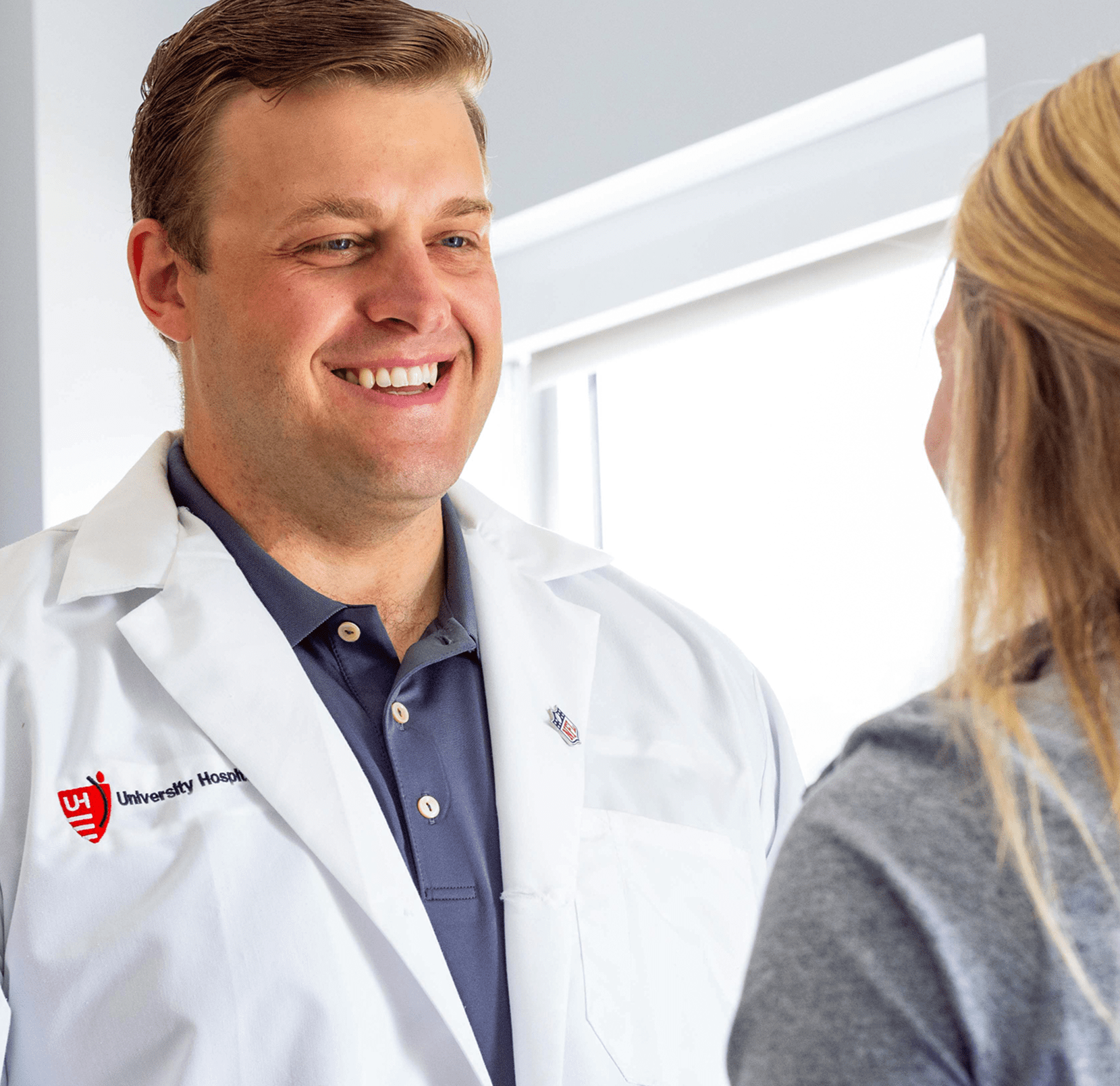 A smiling doctor in a white coat engages in a friendly conversation with a patient in a bright medical setting.