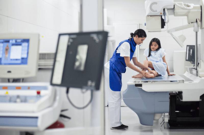 image (23) A radiology technician guiding a patient onto an imaging table inside a medical imaging suite equipped with advanced scan equipment